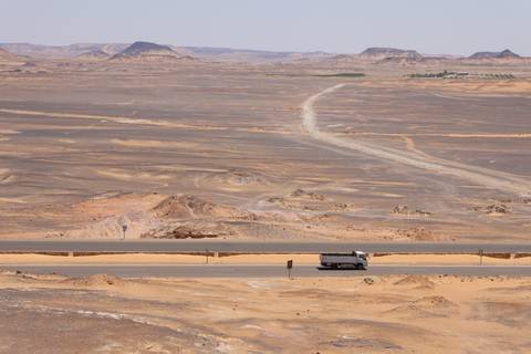      Long desert highway with lone truck winding through barren sandstone plains.
  
