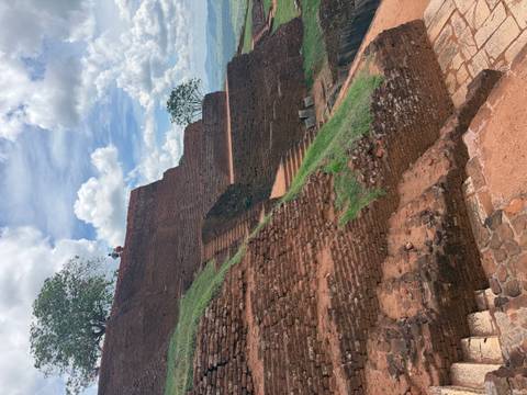       Brick terraces and steps of Sigiriya rock fortress rising against partly cloudy sky.
  