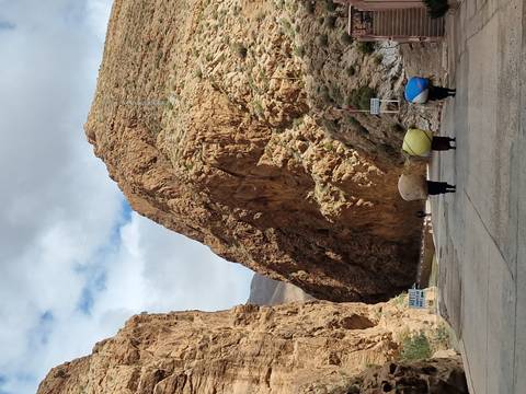      Narrow paved road winding through towering reddish canyon walls with three locals carrying large loads.
  