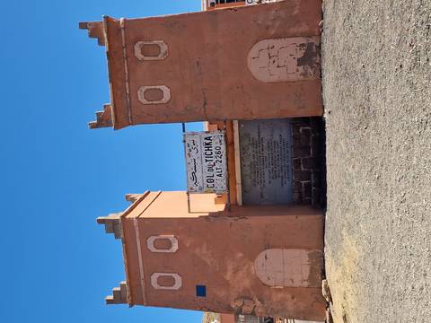       Clay gateway at mountain pass with sign reading "Col du Tichka ALT 2260" against deep blue sky.
  