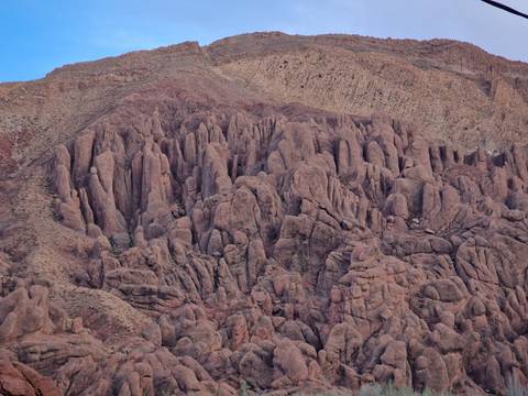       Jagged reddish rock spires and ridges forming dramatic geological patterns on arid mountainside.
  