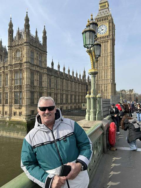       Smiling traveller in sunglasses poses on Westminster Bridge with the neo-Gothic Houses of Parliament towering behind.
  