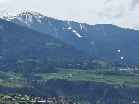       Expansive alpine valley with scattered farms and forested slopes beneath snow-capped mountains.
  