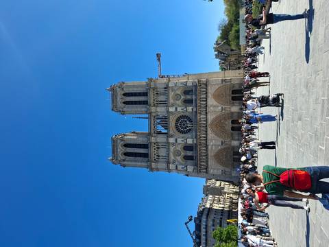       Front view of Notre-Dame Cathedral with many tourists in the plaza under a clear blue sky
  