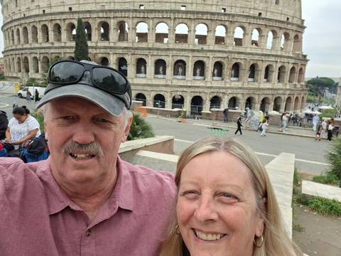       Selfie of a couple with the ancient stone arches of the Colosseum visible behind them
  