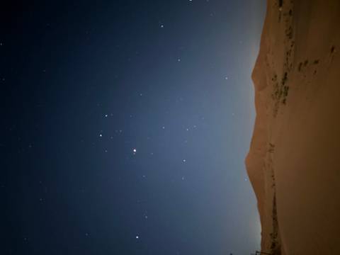       Night desert scene with a starry sky above dark sand dunes
  