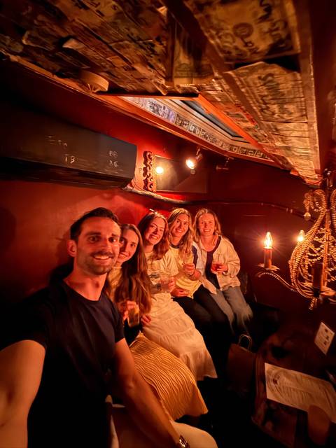       Friends enjoying drinks inside a dimly lit, cozy bar with warm candlelight.
  