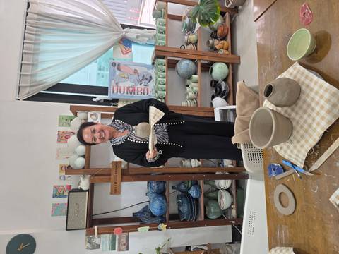       Visitor proudly displaying a freshly made pottery piece in a ceramic studio.
  