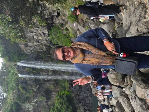       Tourist flashing a peace sign in front of a scenic waterfall crowded with visitors.
  