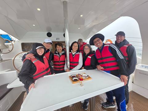       Group of travelers wearing red life vests posing on the deck of a catamaran.
  