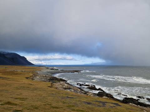      Moody coastal scene with rolling waves and low clouds over a rocky shoreline
  