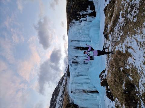       Excited visitor posing in front of an icy waterfall with pastel evening sky
  