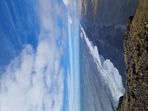       Long aerial view of black sand coastline with white surf and vast blue ocean under scattered clouds
  