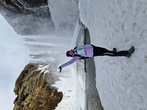       Traveler in winter gear celebrating before a partially frozen waterfall and snowfield
  
