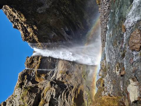       Powerful waterfall crashes between basalt cliffs, creating rainbow mist over a rocky riverbed.
  