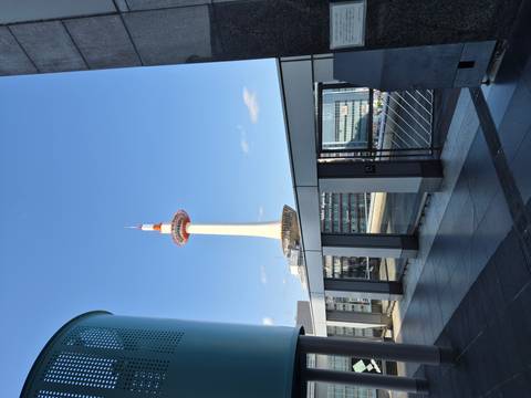       Kyoto Tower rises into a clear blue sky as seen from a modern urban terrace.
  