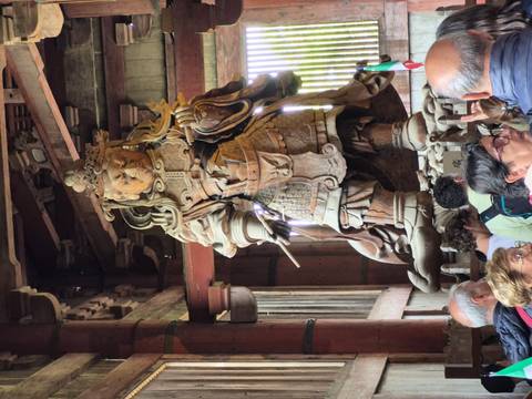       Massive wooden guardian statue towers above visiting crowd inside a historic Japanese temple hall.
  