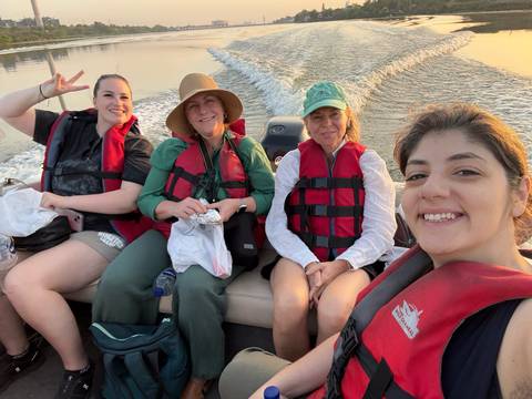       Four travellers wearing life jackets smile for a selfie aboard a speedboat leaving a foamy wake.
  