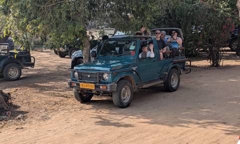       Open-top safari jeep carrying tourists drives through a dusty parking area near the reserve entrance.
  