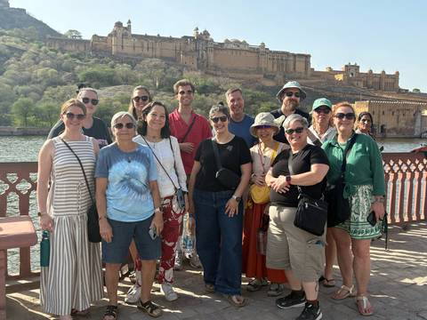       Large tour group poses by a railing with Amer Fort and lake visible in the background.
  