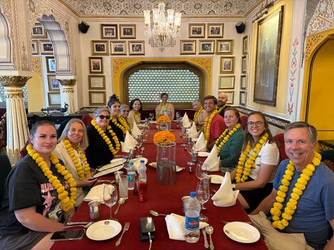       Travellers seated around a long table decorated with marigold garlands in an ornate Indian restaurant.
  