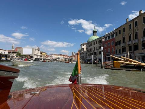       View from a wooden motorboat cruising down Venice's Grand Canal with historic buildings and dome ahead.
  