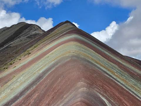       Close-up of the colorful layered strata of Rainbow Mountain under a bright blue sky.
  