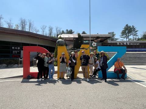       Travelers cheerfully gather before colorful DMZ sign outside visitor center on sunny day.
  