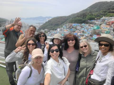       Selfie of smiling group on hilltop overlooking colorful hillside village and harbor.
  