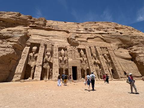       Visitors explore the rock-hewn façade of Abu Simbel under a brilliant blue sky.
  