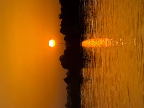       Brilliant orange sun sets over calm Nile waters casting a shimmering reflection.
  