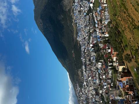       Elevated view of a Moroccan town framed by a forested mountain under a bright blue sky.
  