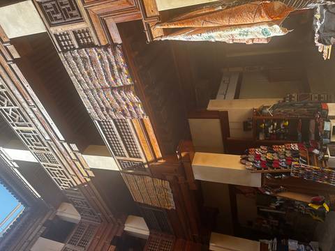       Interior of a traditional Moroccan market building with hanging carpets and slippers for sale.
  