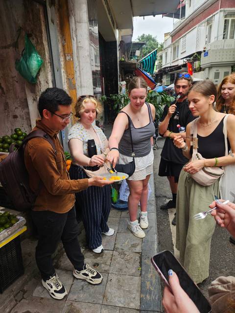      Guide shares a plate of sliced fruit with curious travelers during a bustling street food tour.
  