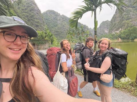       Backpackers posing for a cheerful selfie amid limestone cliffs and a tranquil green lake.
  
