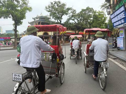      Cyclo drivers pedal tourists through a historic Vietnamese street lined with temples and shops.
  