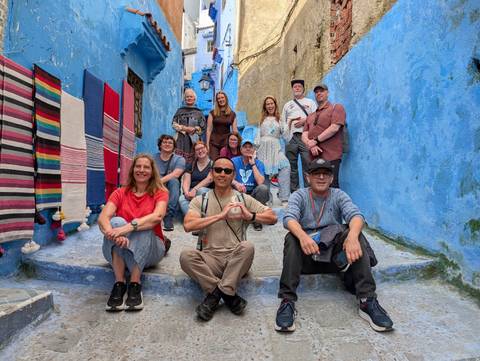       Smiling tour group posing on blue-painted steps in Chefchaouen medina
  