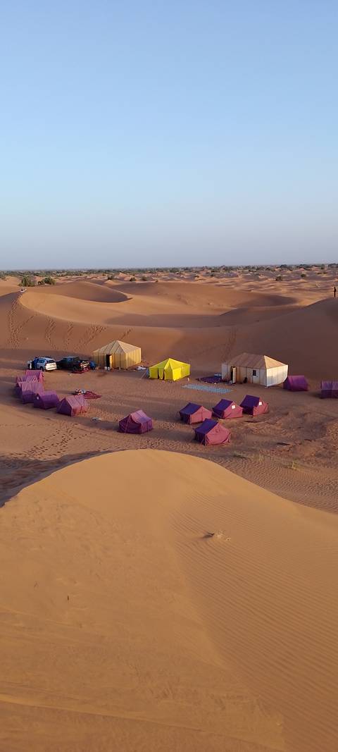       Remote desert camp with rows of purple tents and two larger canvas huts
  