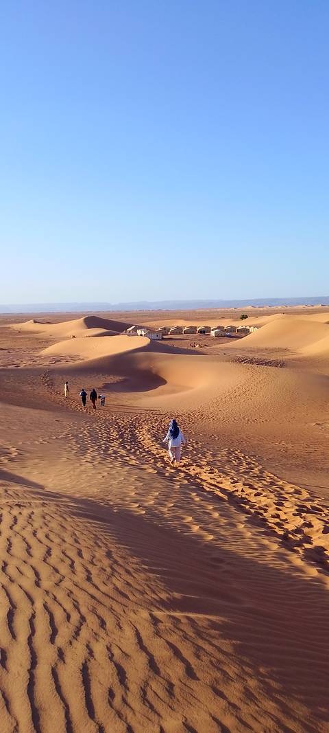       Travellers walking across golden dunes toward a desert camp at sunrise
  