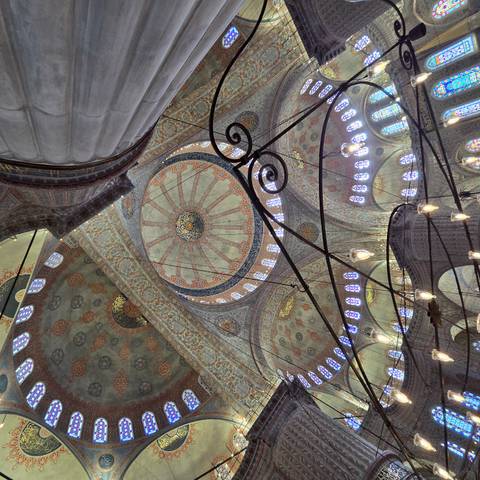       The richly decorated interior dome and stained-glass windows of Istanbul’s Blue Mosque captured from below.
  