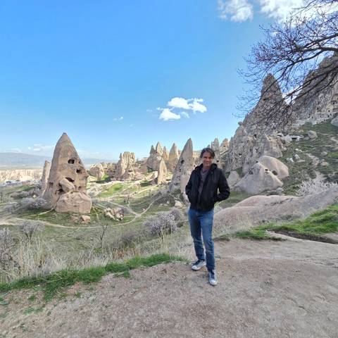       A traveler poses among Cappadocia’s distinctive fairy-chimney rock formations under a clear blue sky.
  