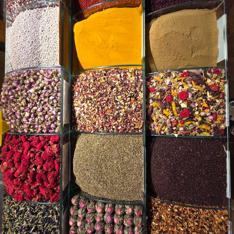       Colorful rows of dried herbs, teas, and spices neatly displayed in glass bins at a market stall.
  