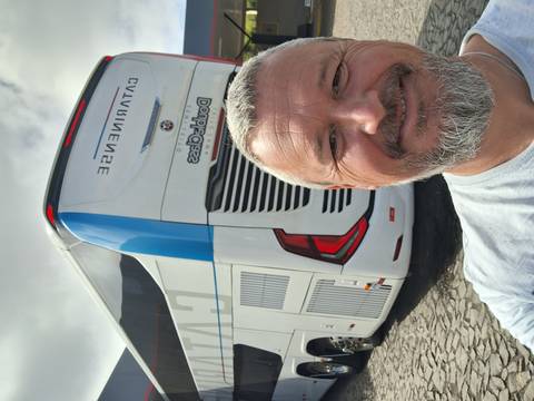       Smiling man takes a selfie with a modern touring coach parked behind him
  