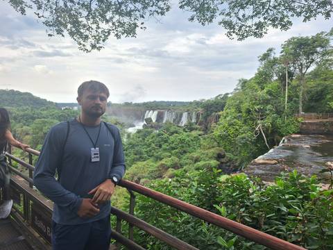       Young man stands at balcony viewpoint overlooking the powerful waterfalls and lush jungle of Iguazu
  