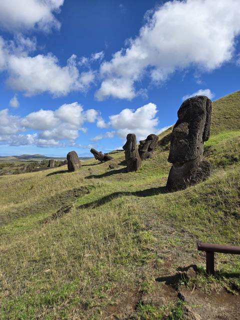       Row of partially buried Moai statues on grassy slope under blue sky and scattered clouds
  