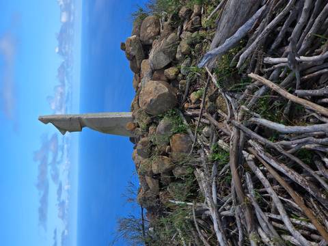       Modern stone sculpture resembling a Moai stands on rocky cairn overlooking vast ocean
  