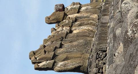       Side view of a long row of iconic Moai stone statues standing on a stone platform under a blue sky
  