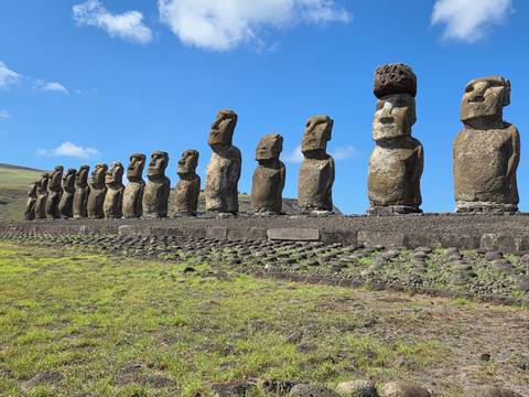       Front view of multiple Moai figures lined up on a stone ahu with grassy foreground under bright blue sky
  