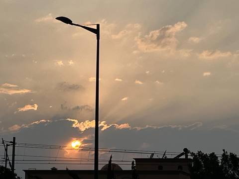       Hazy sunset with sun peeking beneath clouds and a silhouetted streetlamp.
  