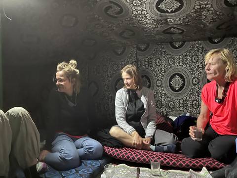       Three women chat inside a patterned Bedouin tent at night.
  